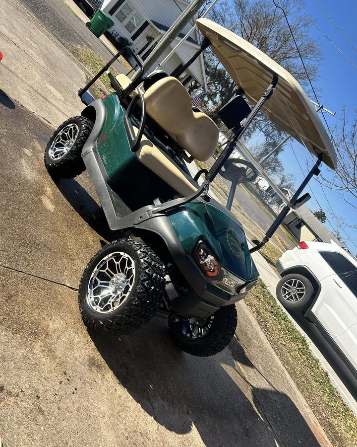 Green golf cart on lifted wheels in a driveway after a wash