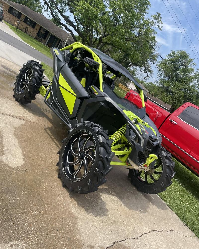 Green and black Can-Am side-by-side on mud tires in a driveway after a wash