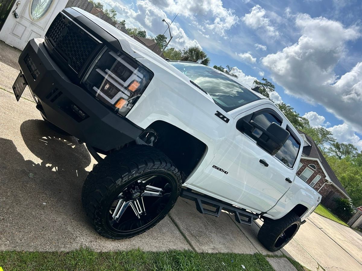 White lifted Chevy Silverado HD on black wheels in a driveway after a detail, paint and tires spotless